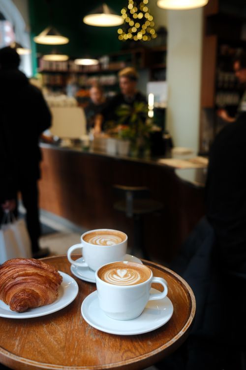 Free Warm cafe ambiance featuring lattes and a croissant on a wooden table, perfect for a cozy coffee shop vibe. Stock Photo