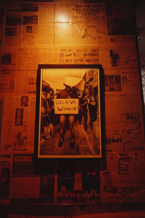 Free A striking photograph of a 'Believe Women' protest sign framed on a newspaper-covered wall. Stock Photo