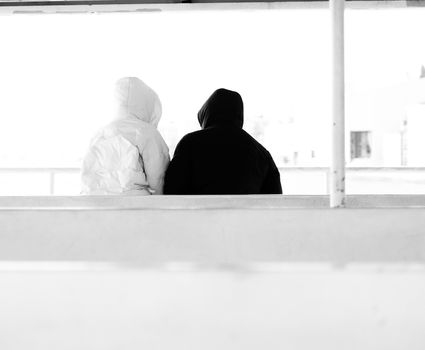 Minimalist black and white photo of two individuals sitting, wearing hooded jackets.