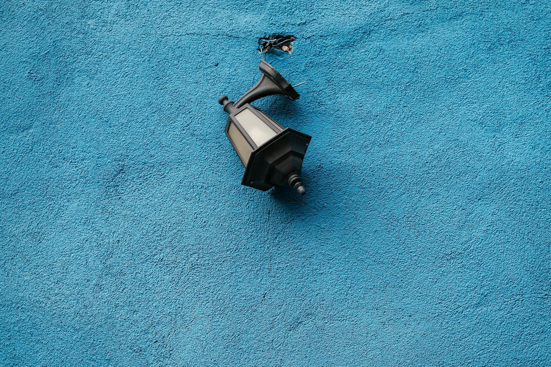 A damaged wall lantern against a bright blue textured surface in daylight.