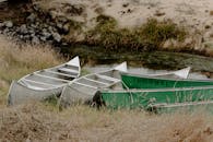 夏日，三艘划艇停靠在长满青草的河岸上，展现出宁静的乡村风光