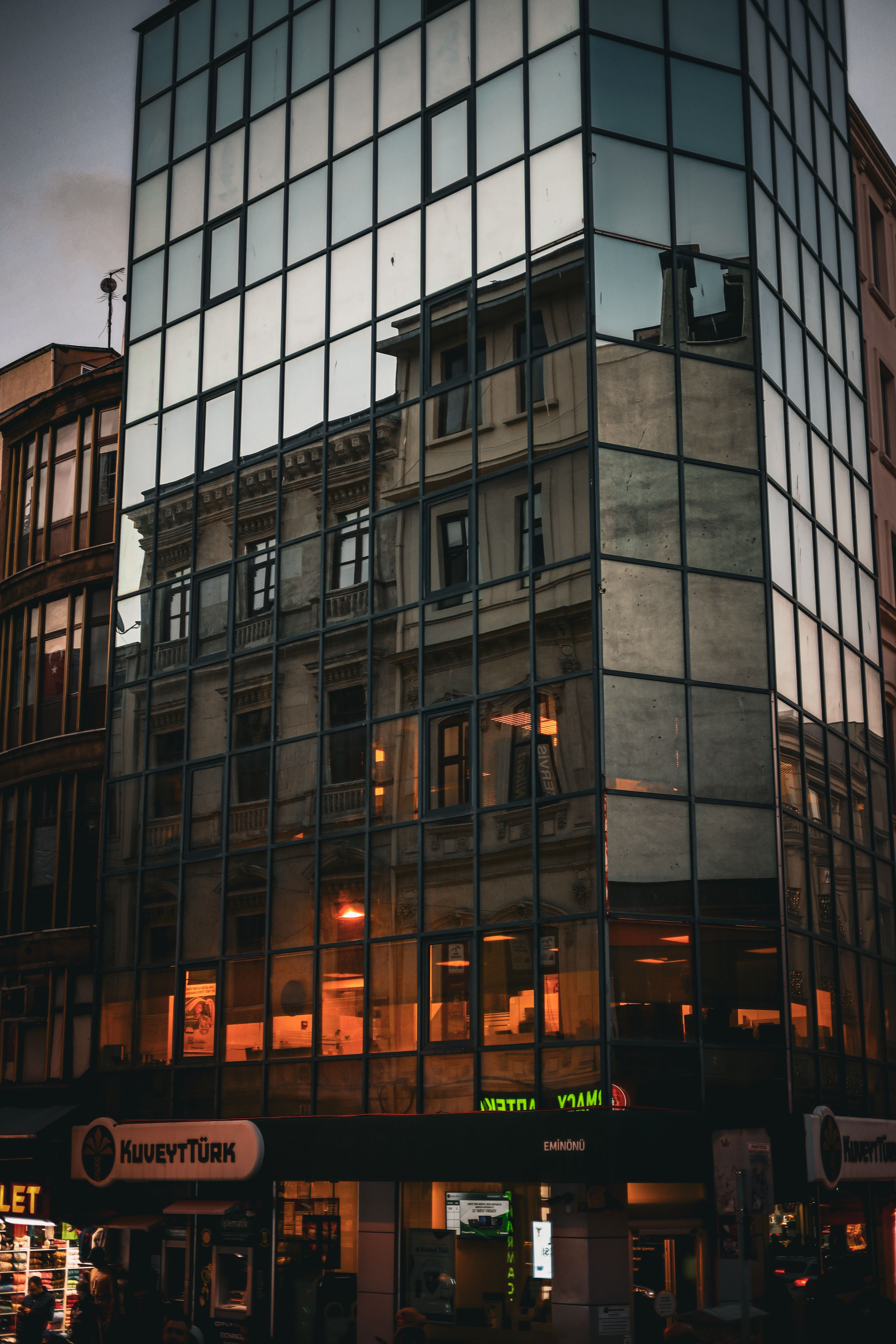 A modern glass building reflecting an old structure at dusk, blending architecture styles.