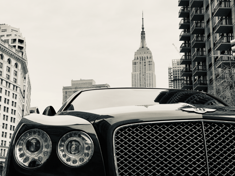 A striking black luxury car set against a bustling cityscape and iconic skyscraper.