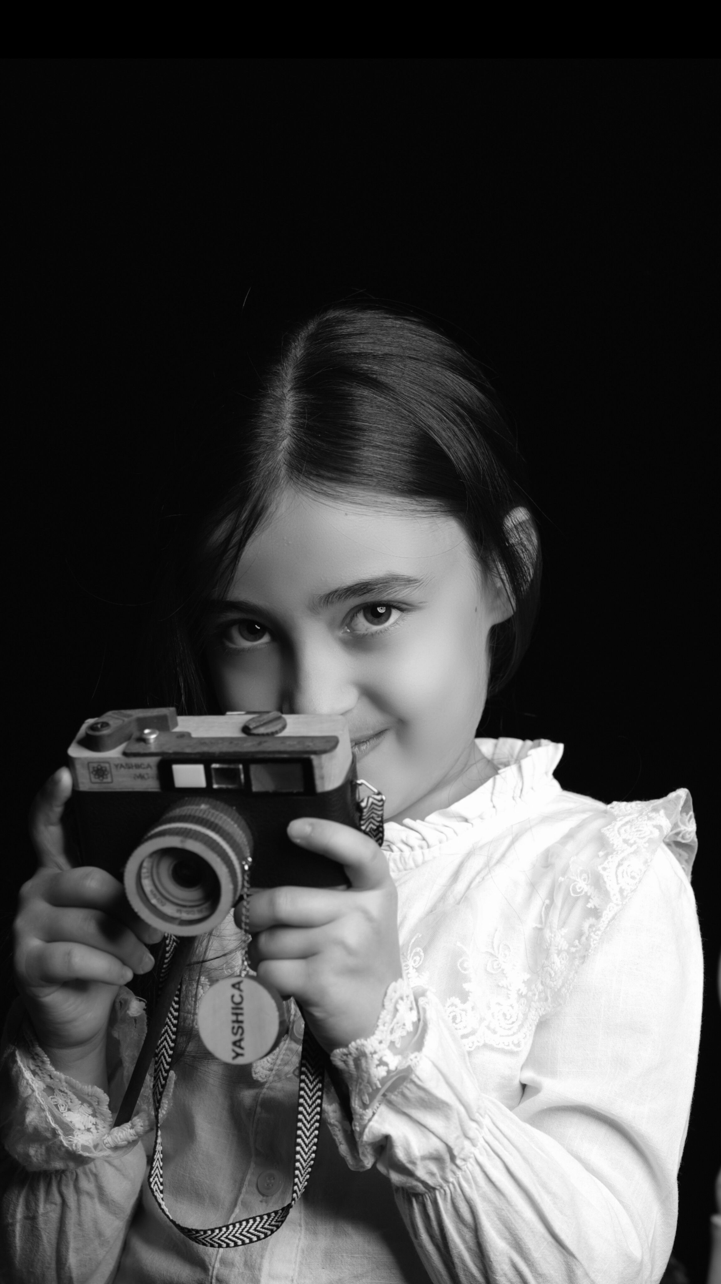 Charming young girl with a vintage camera, black and white portrait.