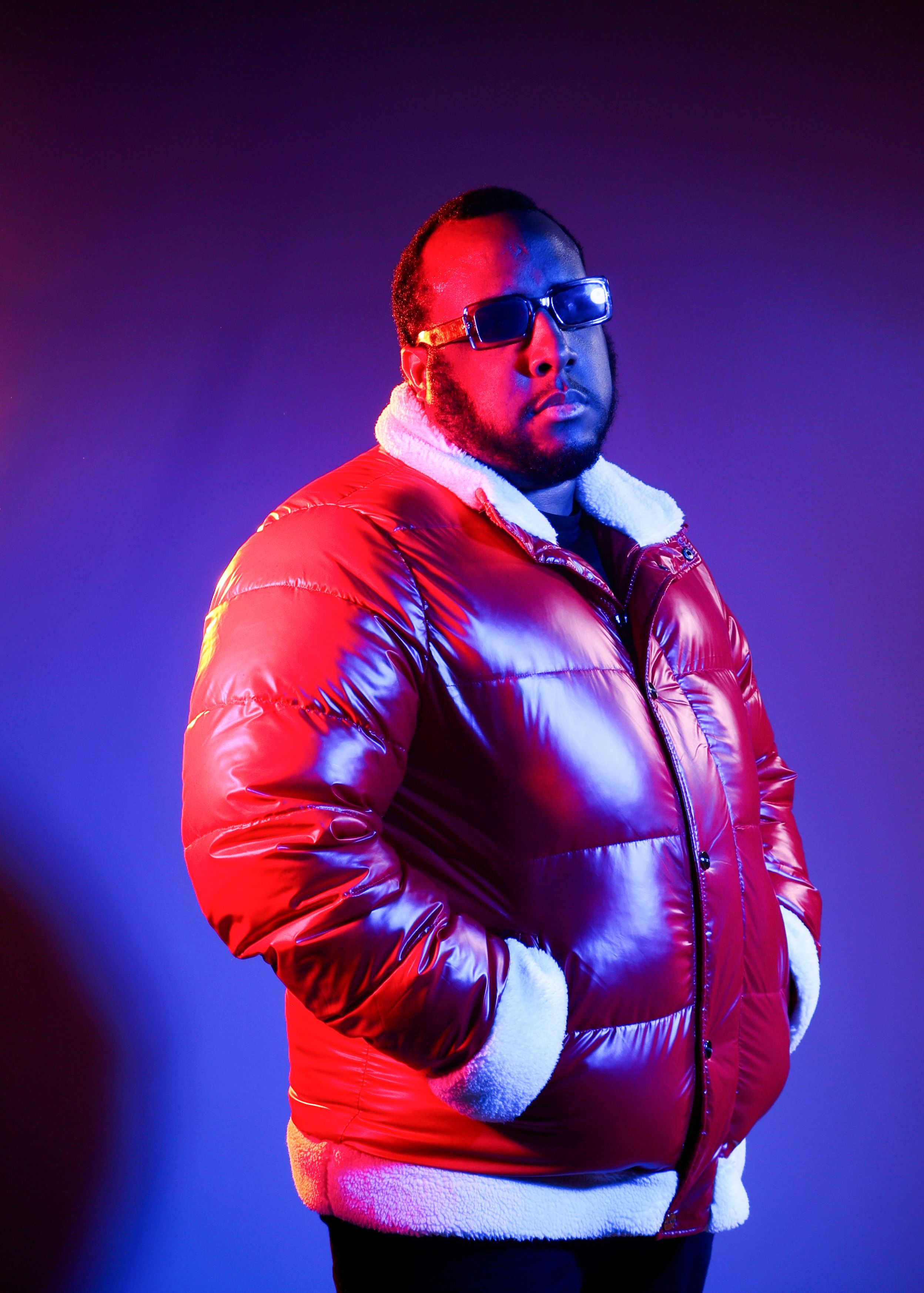 Male model wearing a red puffer jacket poses confidently against a purple studio backdrop.