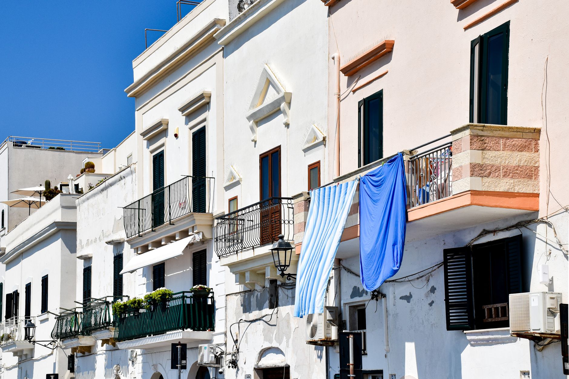 Charming whitewashed buildings with colorful laundry in Apulia, Italy under a bright blue sky.