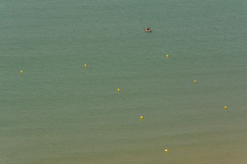 Free Lone kayak amidst yellow buoys on calm green water, seen from above. Stock Photo