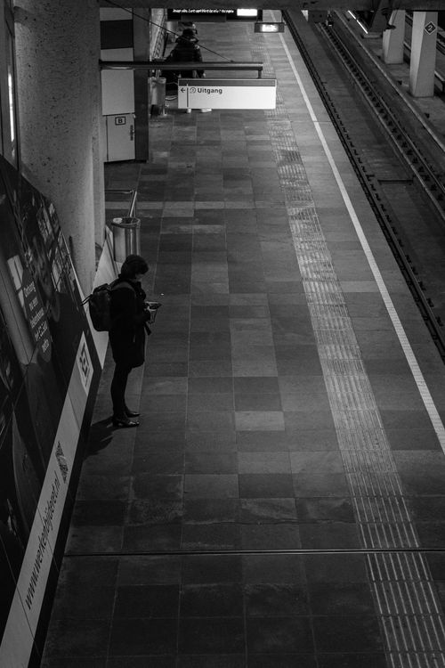 Free Black and white image of a solitary figure waiting at an empty subway platform. Stock Photo