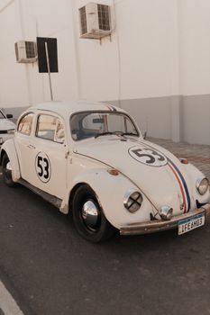 Vintage Volkswagen Beetle car with racing decals parked on an urban street under warm lighting.