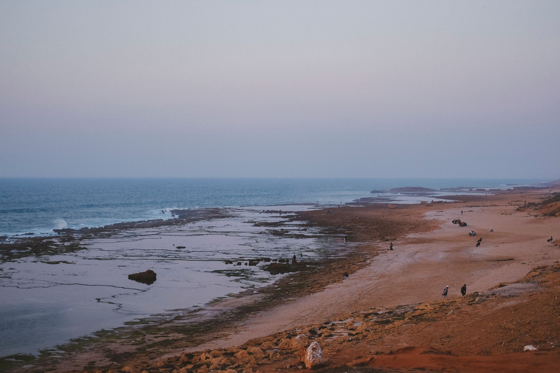 Tranquil sunset view over Oudayas Beach in Rabat, Morocco with scattered visitors along the shore.