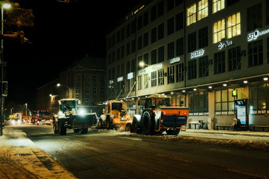 Snow plows clearing city streets at night during winter, urban setting.