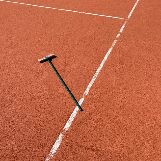 A minimalist image of a clay tennis court with a line brush creating distinct white lines under clear daylight.