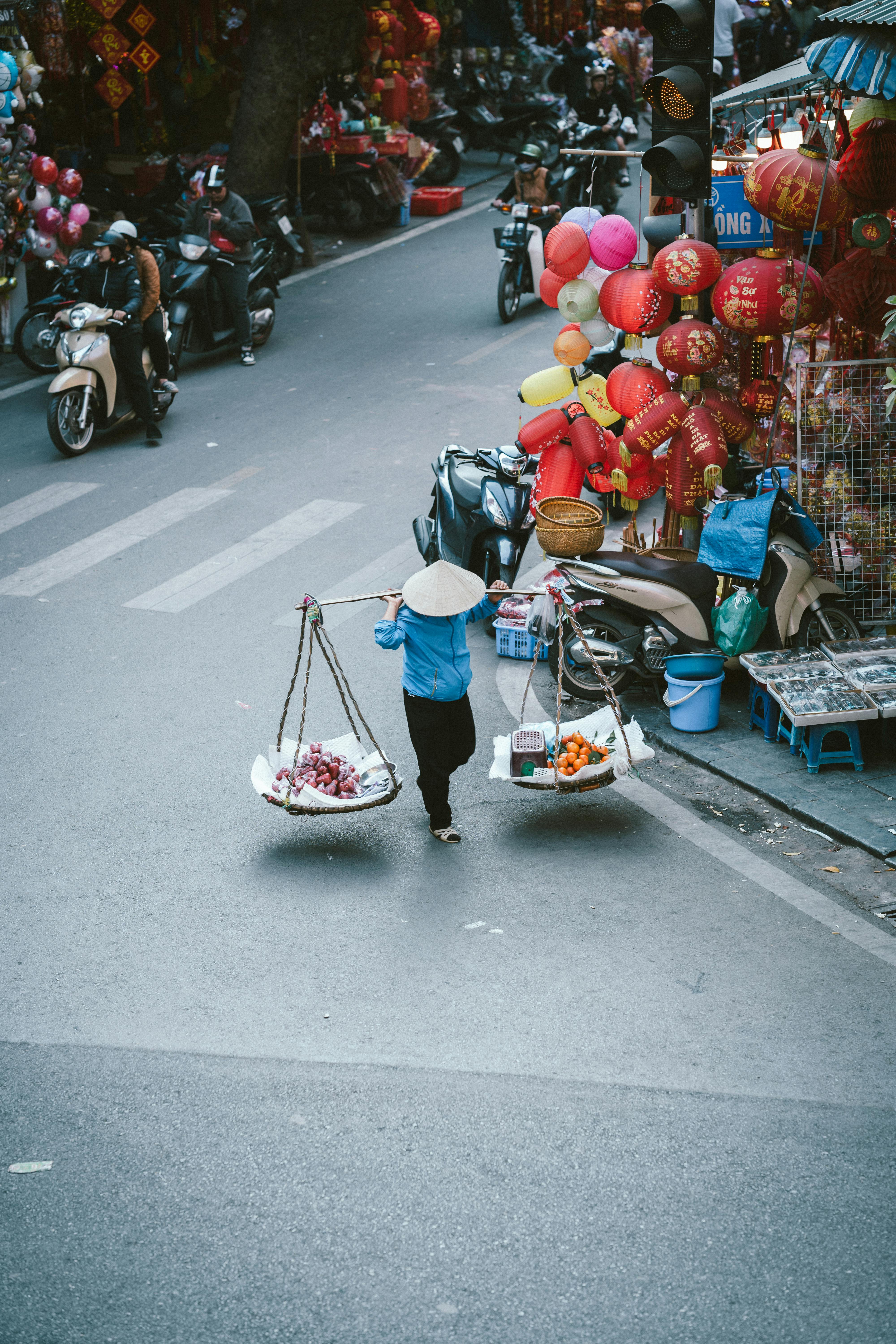 Colorful street scene in Hanoi with a traditional vendor carrying baskets on a bustling road.