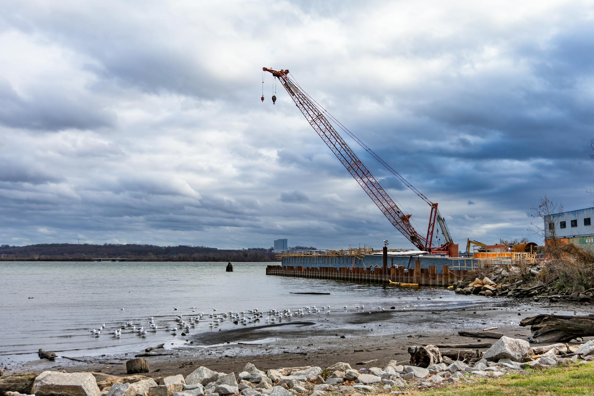Crane on a waterfront construction site under dramatic cloudy skies.