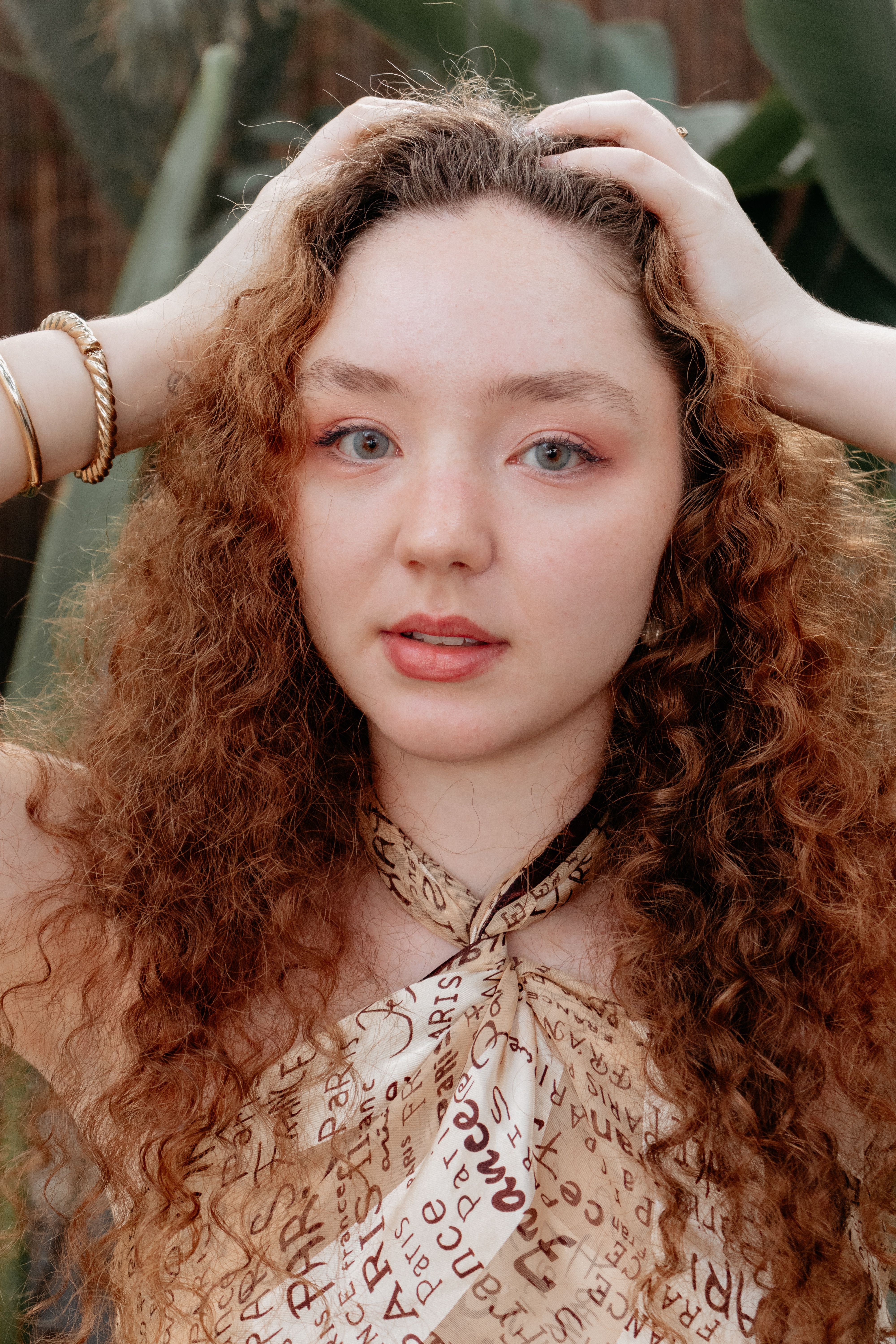 A close-up portrait of a young woman with curly hair in an outdoor setting, exuding warmth and style.