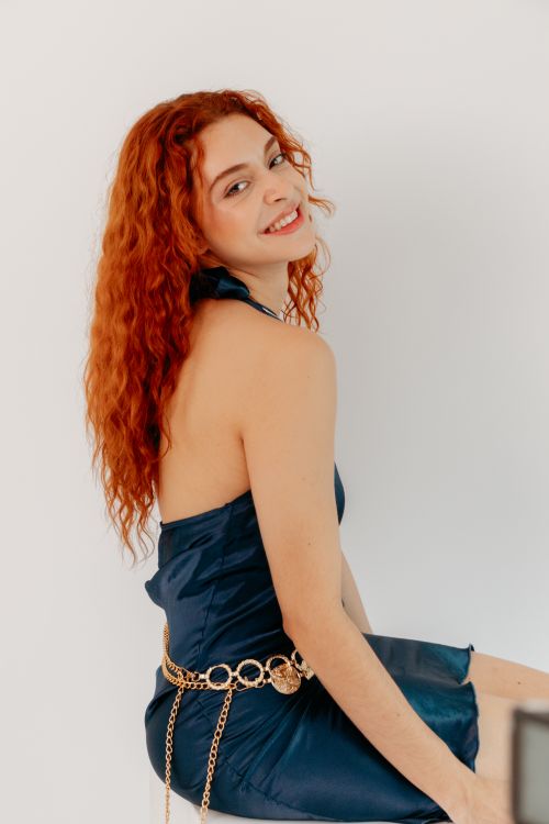 Free A stylish woman with red hair wearing a blue dress and smiling against a white background. Stock Photo