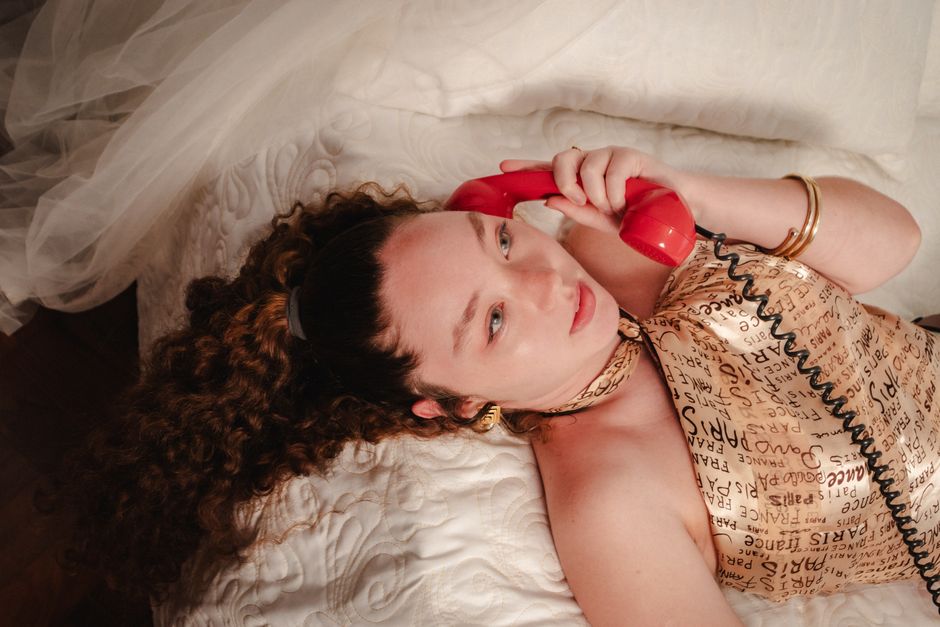 Woman reclining and talking on a red vintage telephone indoors.