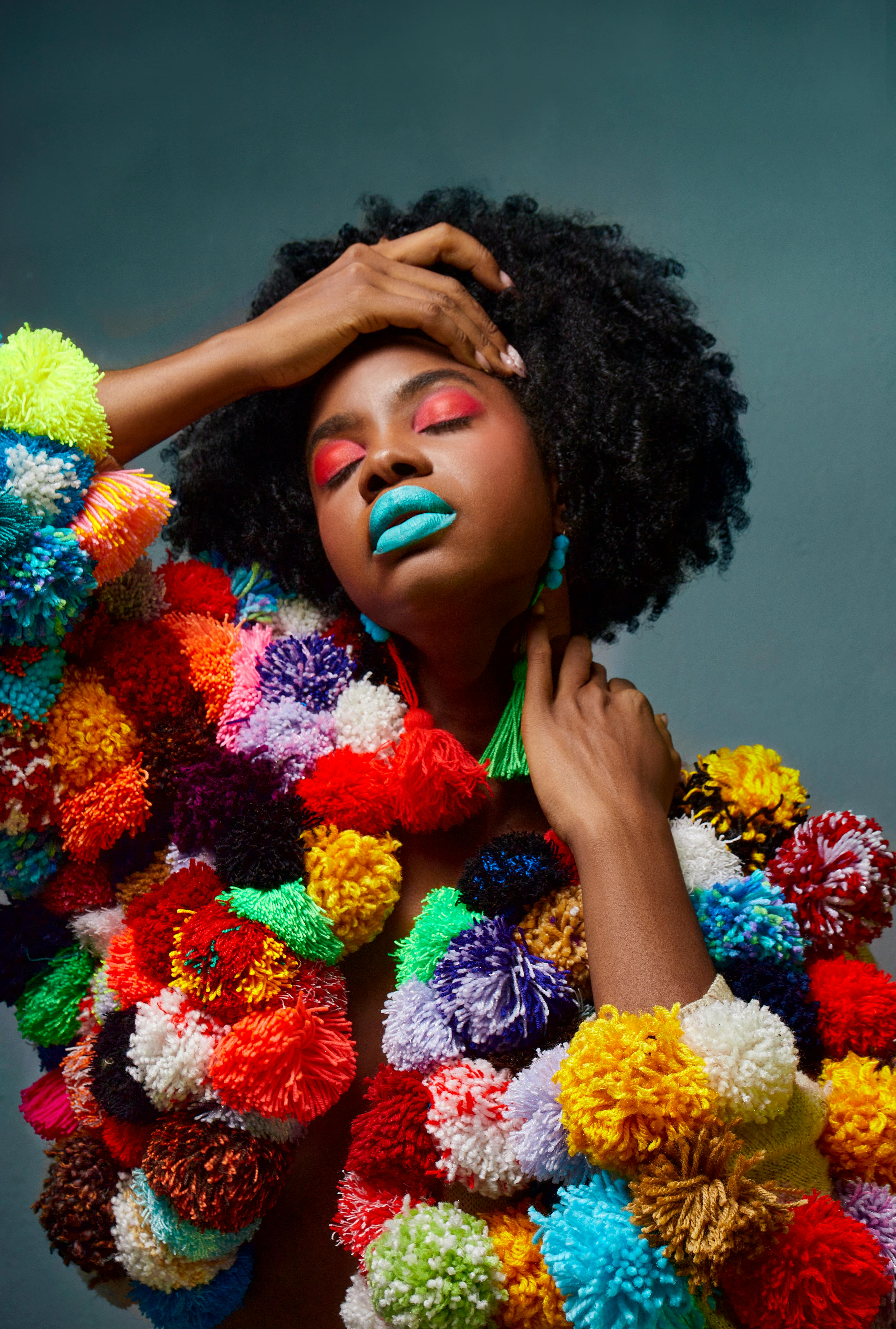 Striking portrait of a woman wearing a colorful pom pom jacket with bold makeup.