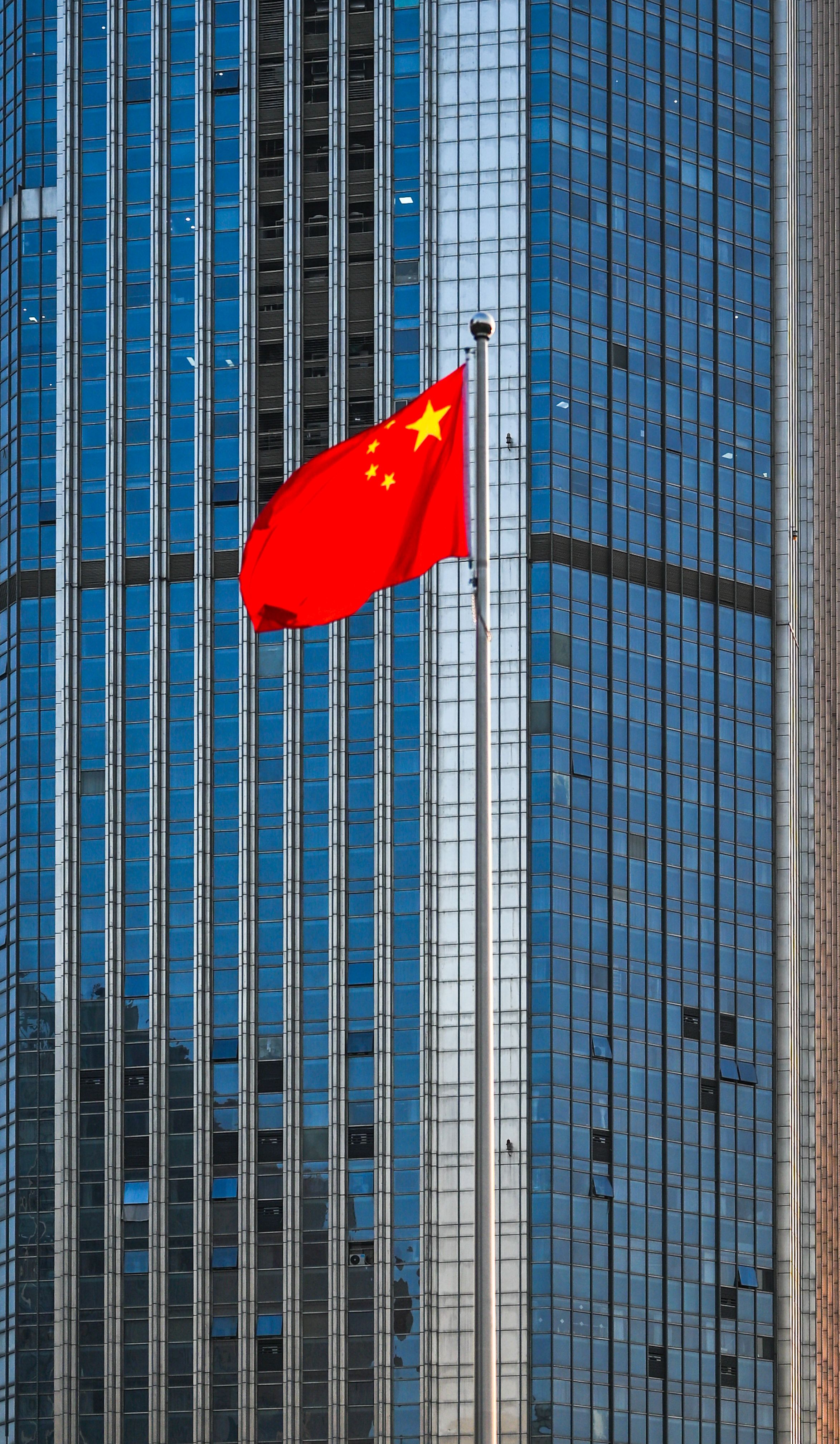 Chinese national flag waving in front of a modern skyscraper, symbolizing urban progress.