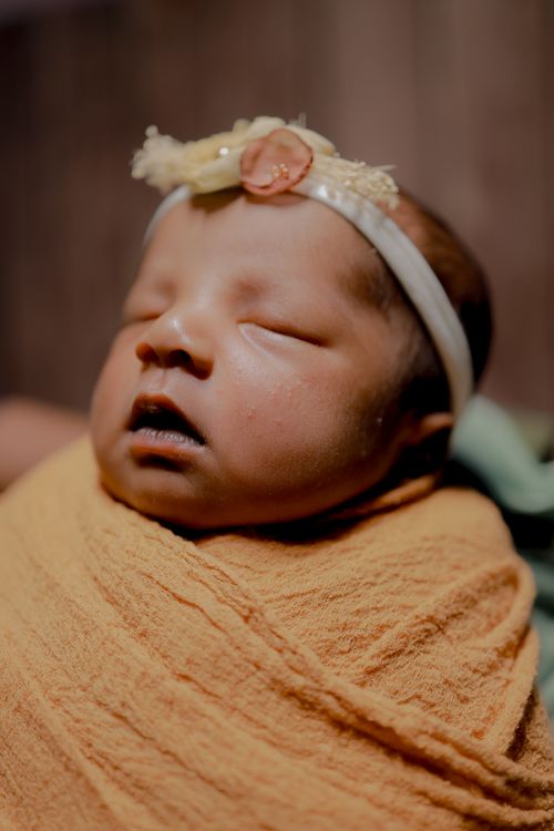 Free Close-up of a serene sleeping newborn wrapped in a yellow blanket with a decorative headband. Stock Photo