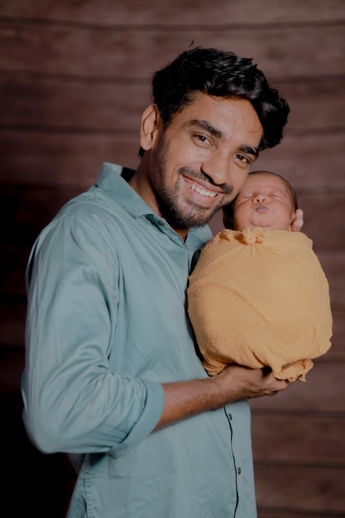 Free A joyous father holding his newborn baby wrapped in a yellow blanket indoors. Stock Photo