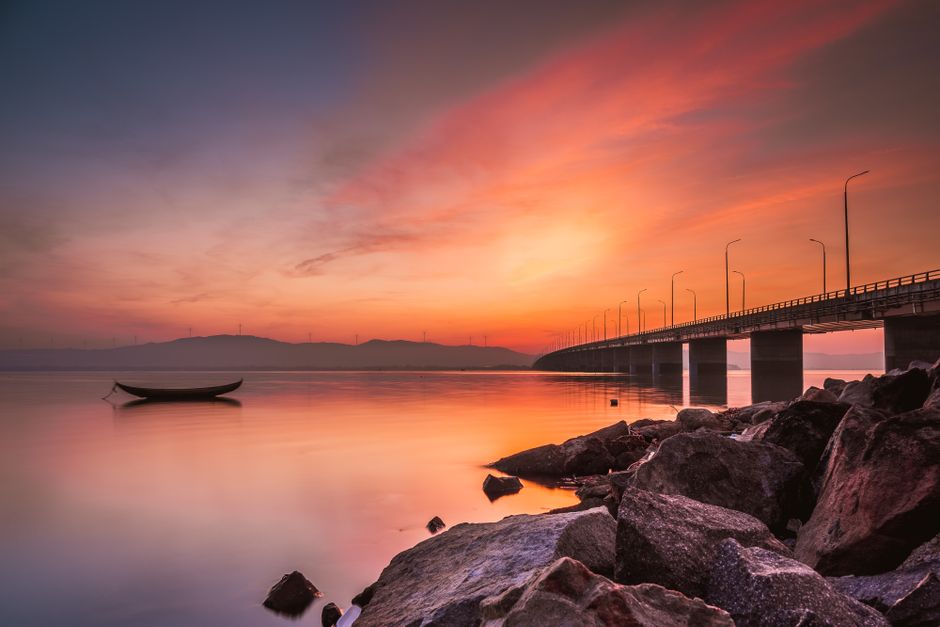 Beautiful sunset over Quy Nhơn beach with a tranquil boat and modern bridge.