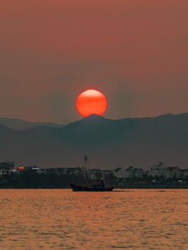 Stunning sunset view across Quy Nhơn bay with silhouetted mountains and a fishing boat.