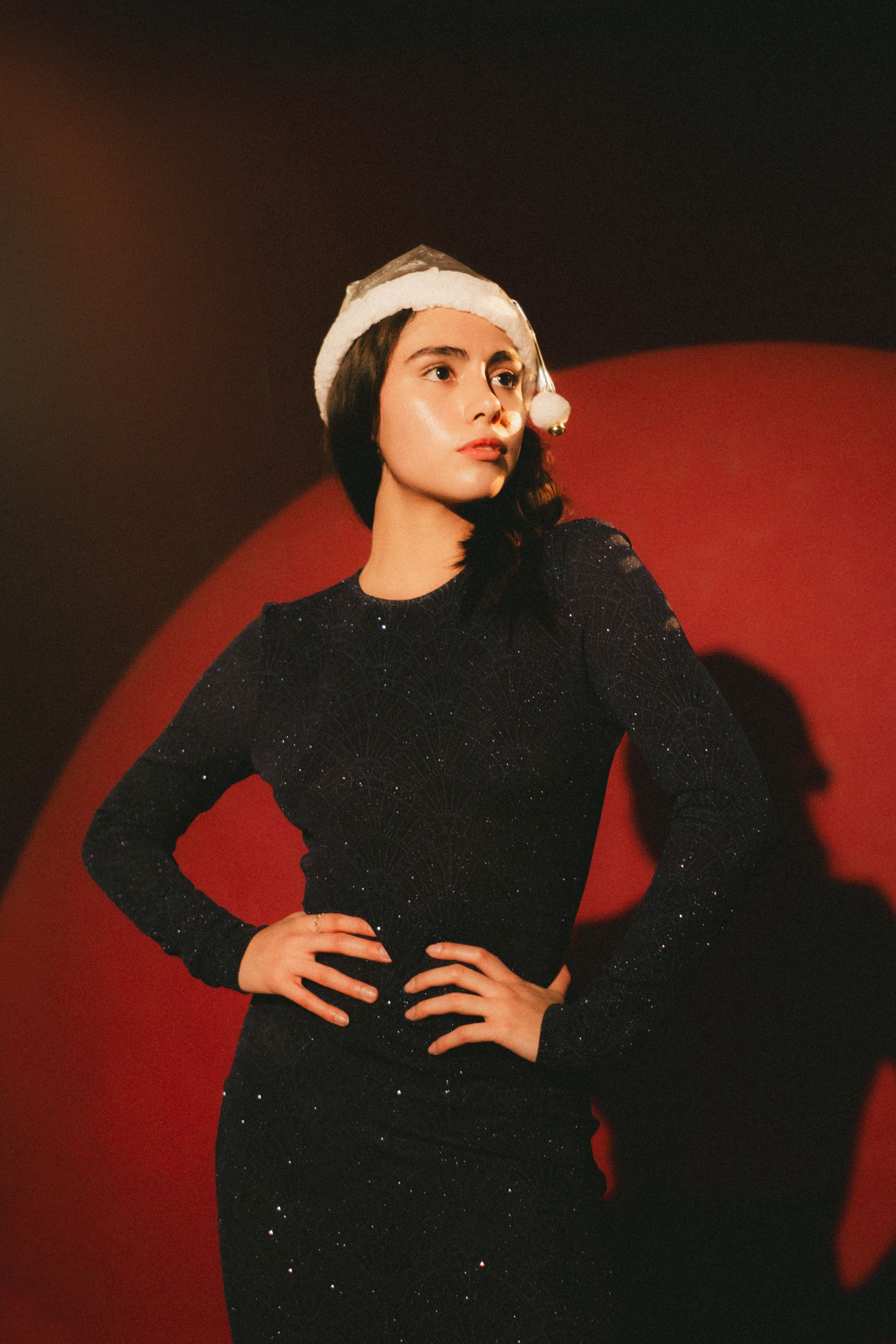 Stylish woman in Santa hat against a red backdrop, embodying festive cheer.