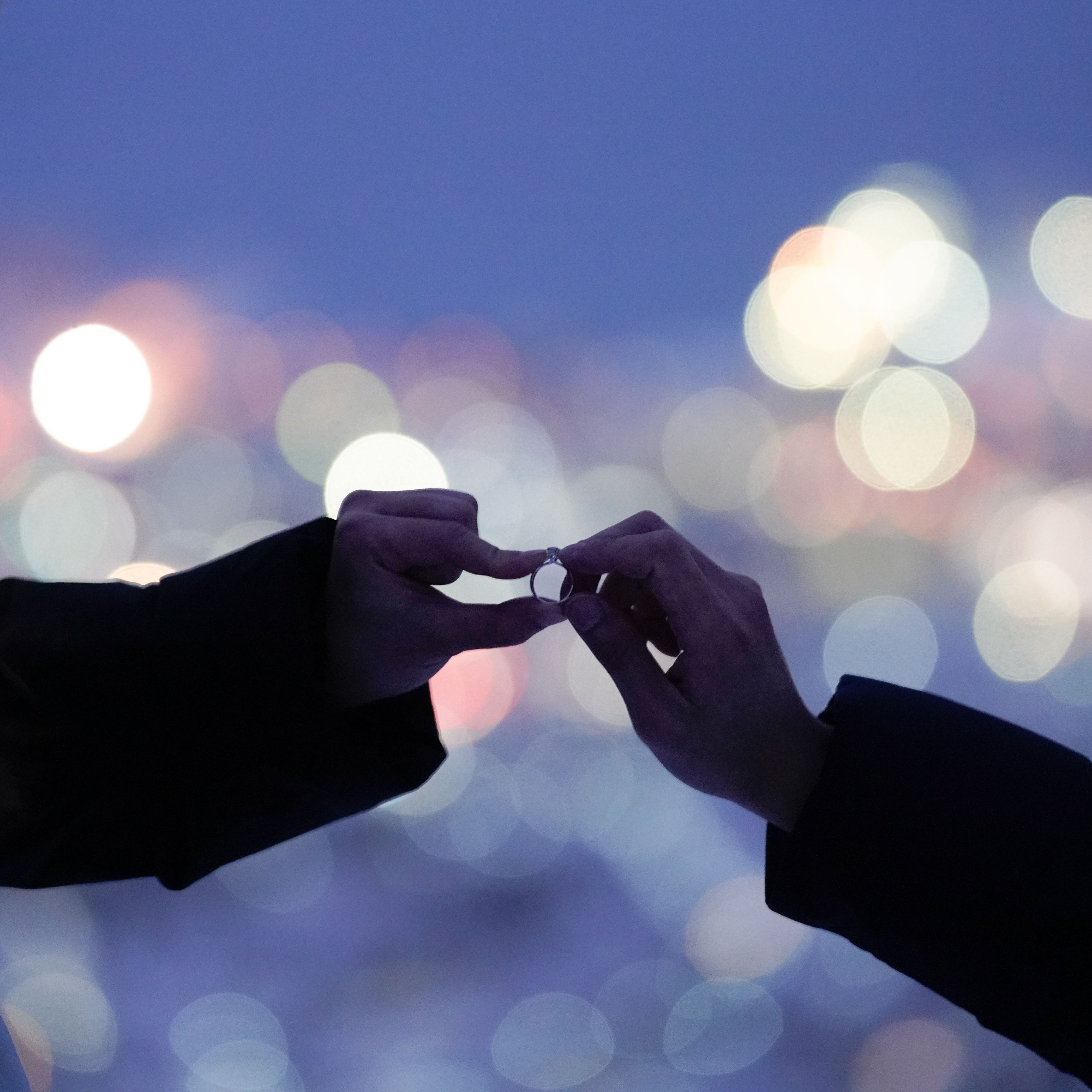 A romantic proposal with hands exchanging a ring against a city bokeh background.