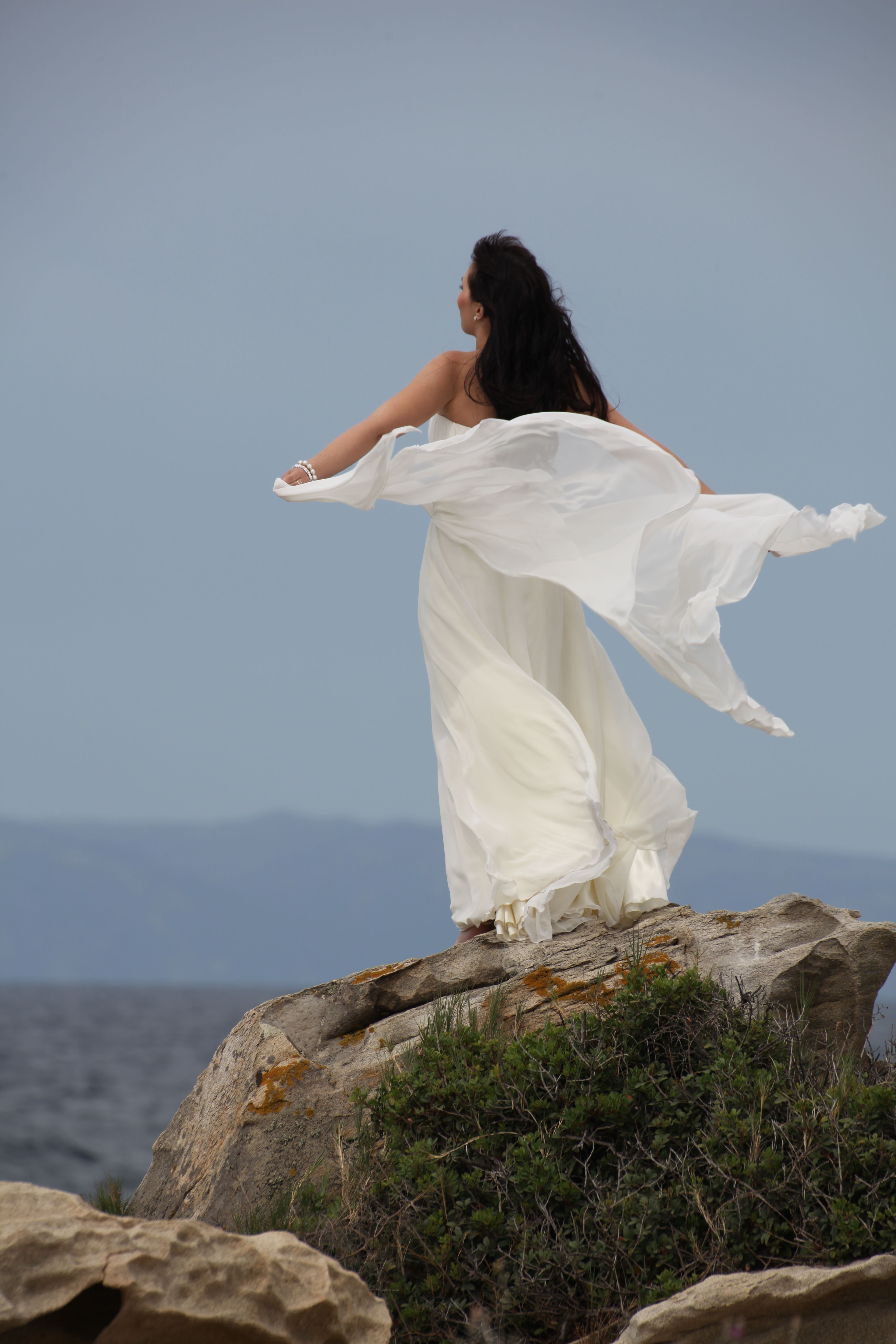 Woman in Flowing White Dress on Coastal Rocks · Free Stock Photo