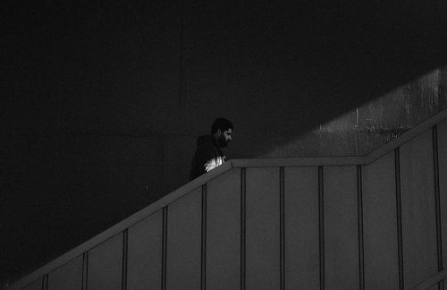 Free Black and white image of a man ascending a staircase, creating a dramatic shadow play. Stock Photo