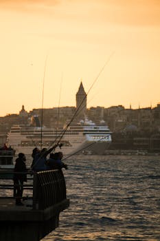 Silhouetted fishermen casting lines at sunset near a cruise ship.