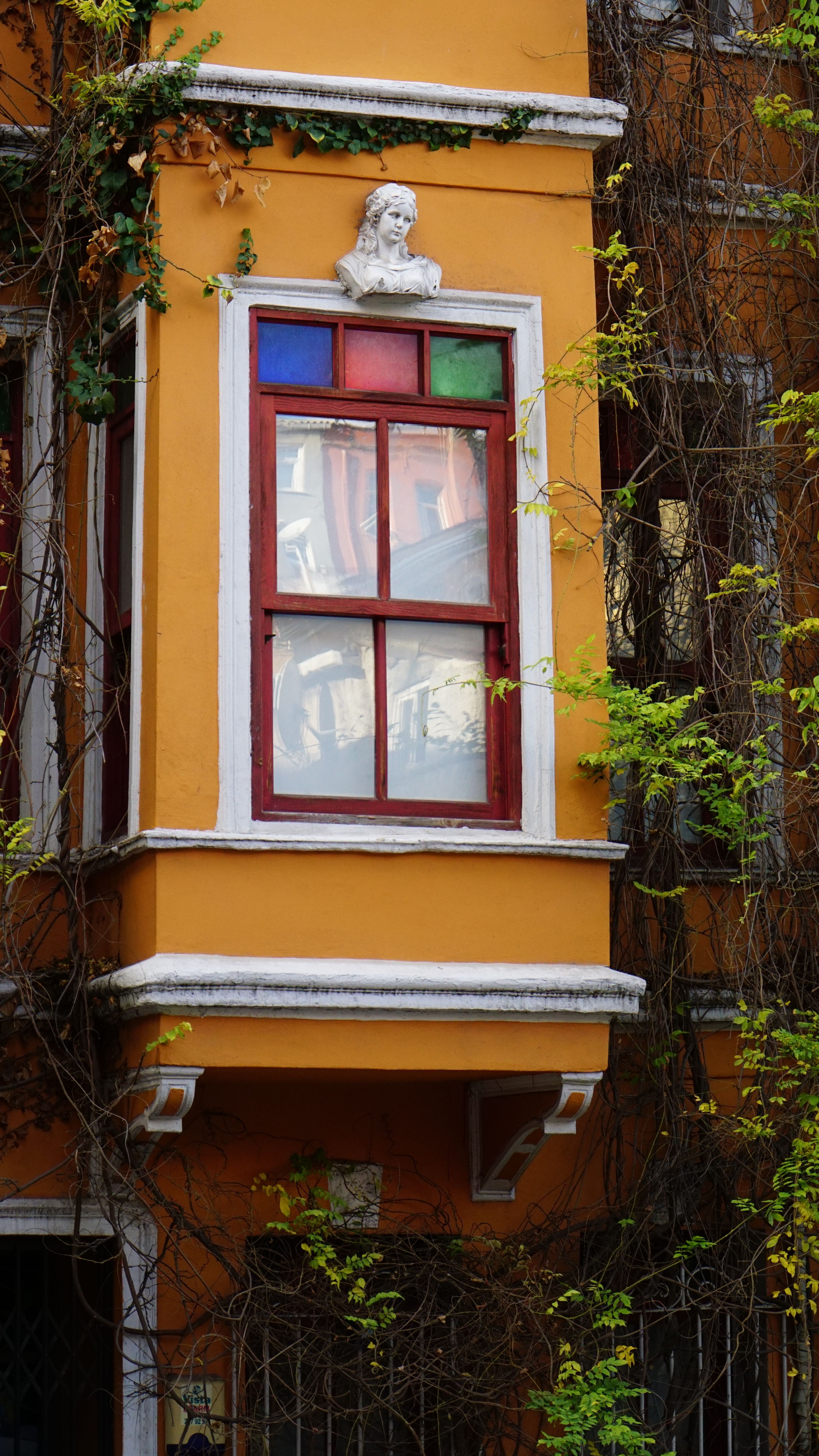 Vibrant orange building facade with a colorful window in Istanbul's historic area, adorned with ivy and architectural details.
