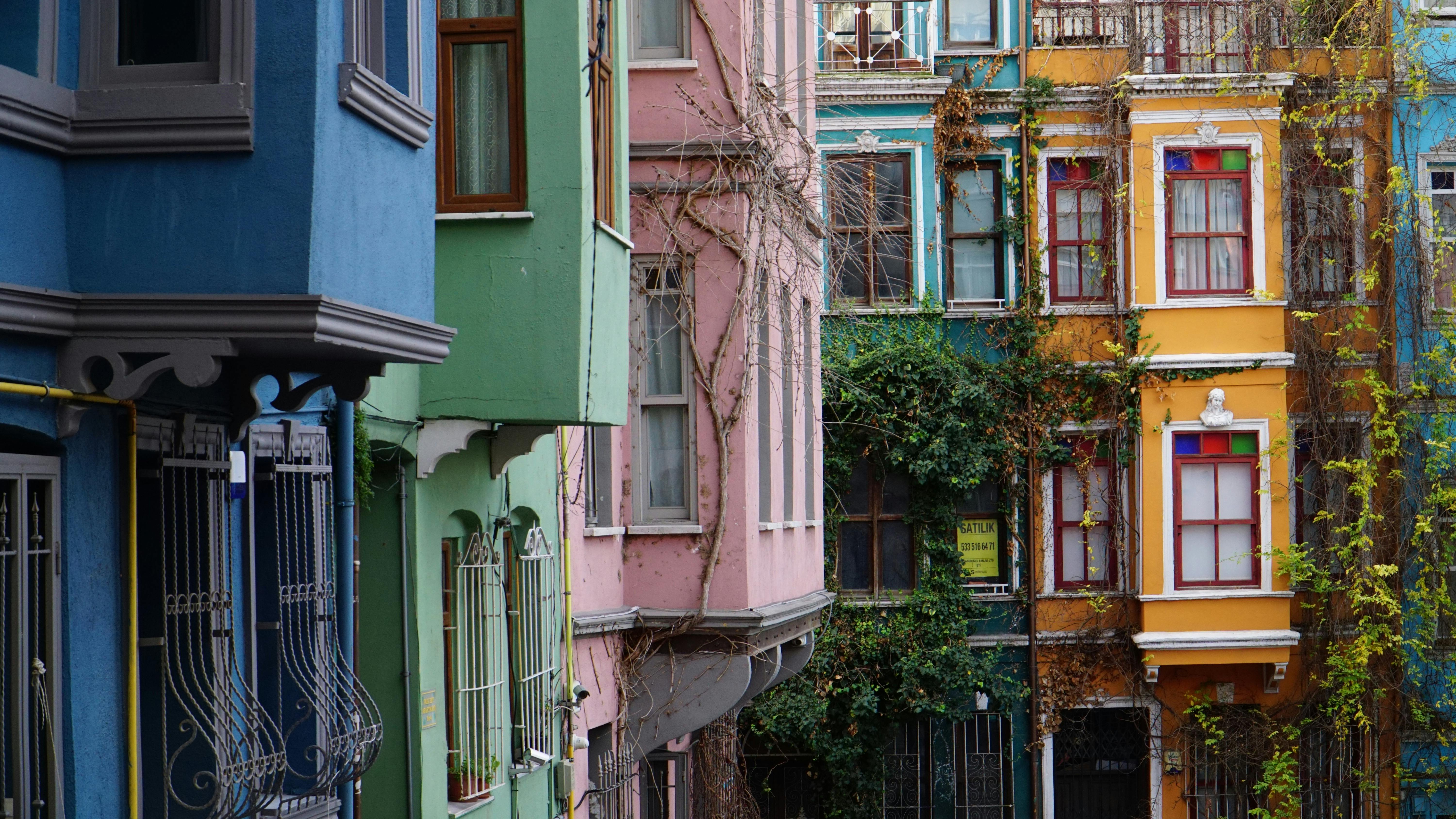Close-up of vibrant, multi-colored historic buildings with ornate windows, balconies, and climbing vines, creating a picturesque urban street scene.