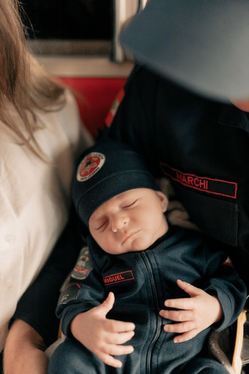 Free Adorable baby asleep in firefighter attire, embraced by parents. Stock Photo