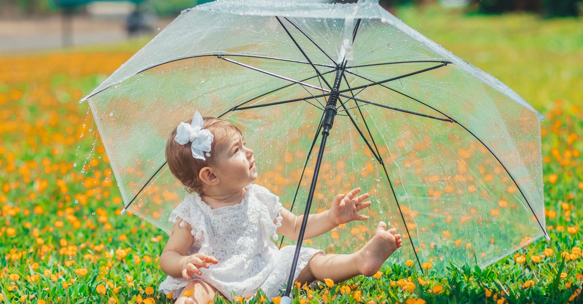 夏の日差しの下、透明な傘の下で花に囲まれて座る赤ちゃんのイメージ