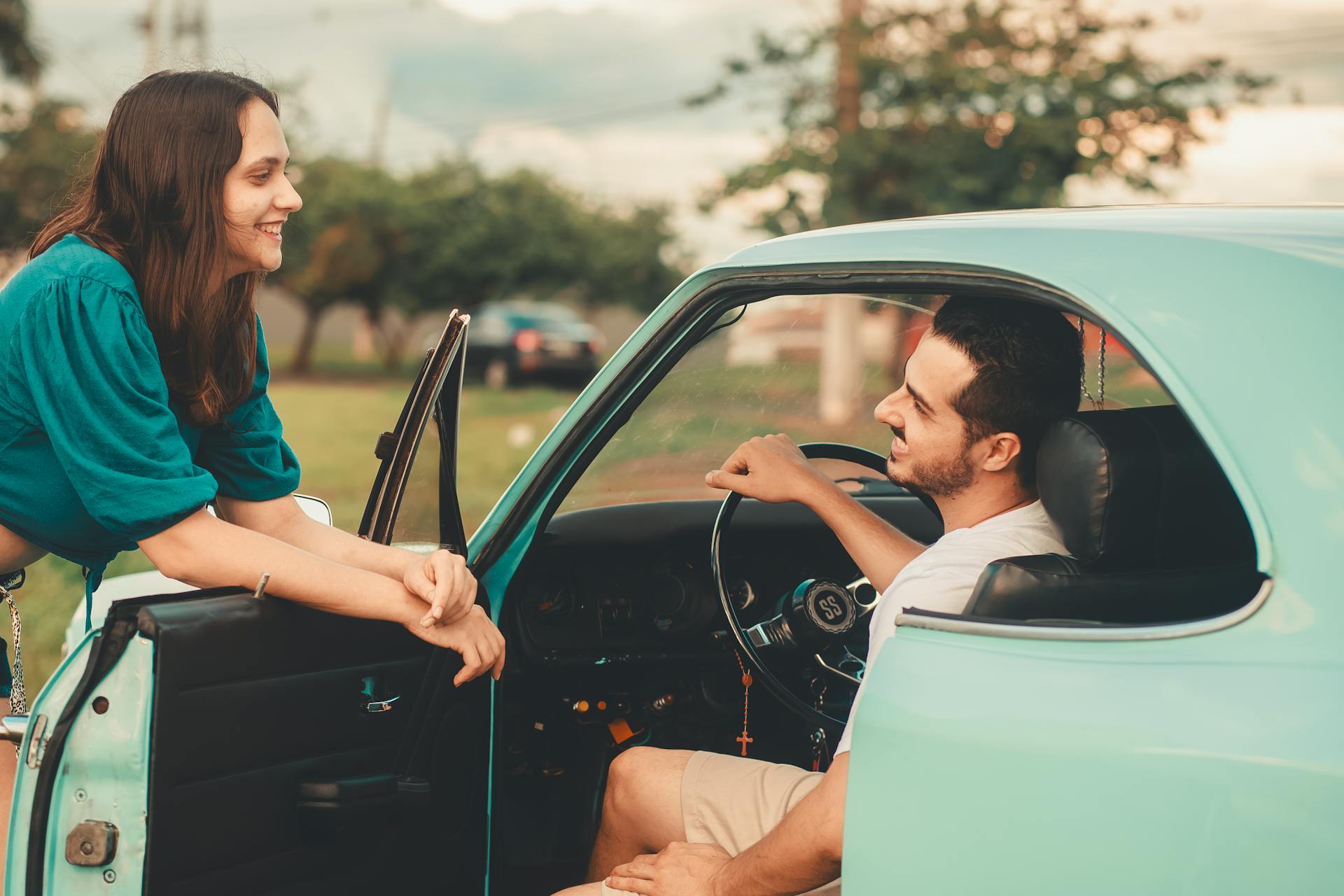 A cheerful young couple enjoys their time together by a classic car outdoors during the day.