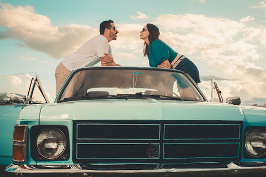 A couple leaning on a vintage convertible car under a bright sky, exuding a vintage romance vibe.
