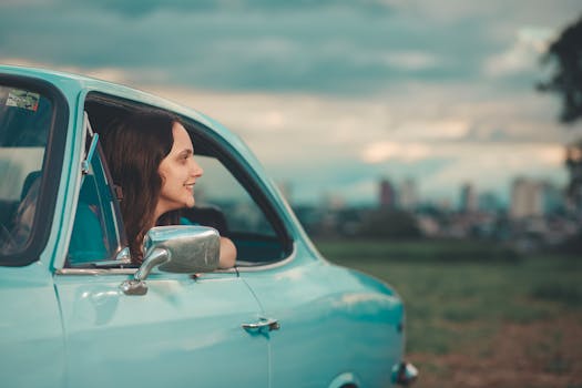 A woman smiles from a vintage car window enjoying a scenic outdoor view.