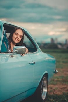 Cheerful woman leaning out of a vintage blue car on a countryside road.