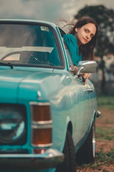 Woman leaning out of a classic blue car on a scenic outdoor day, evoking a sense of freedom.