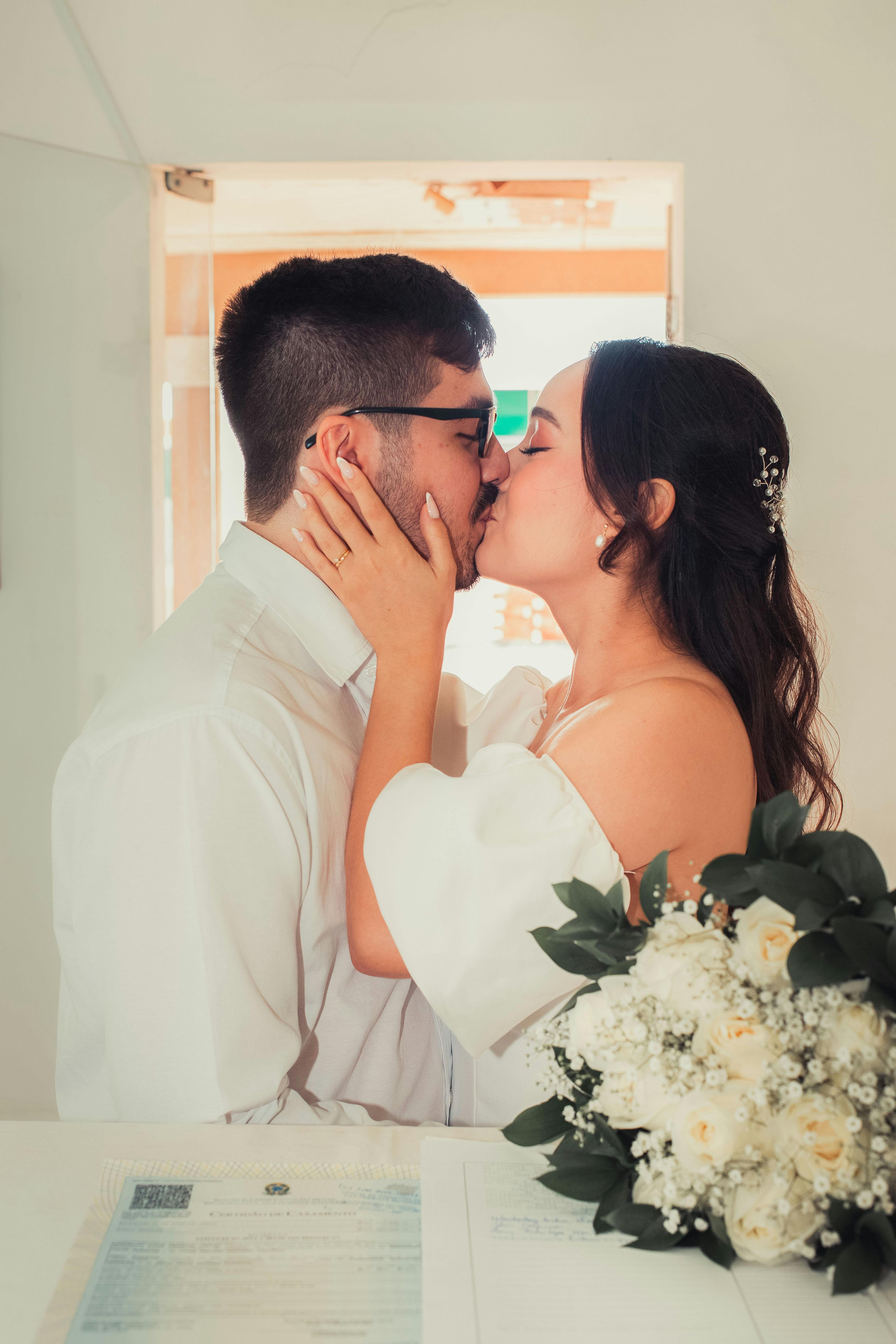 免費 新娘和新郎在室內婚禮上手捧花束，分享浪漫的吻。 圖庫相片