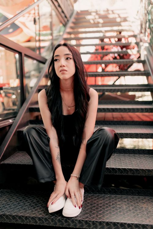 Free Stylish woman with long hair sitting on metal stairs in an urban setting. Stock Photo