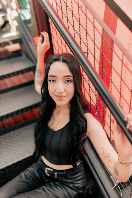 Free Stylish woman with tattoos sits on a colorful urban staircase, exuding confidence. Stock Photo
