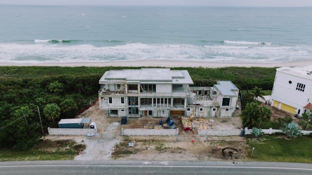 Aerial shot of a house under construction near the ocean with lush greenery.