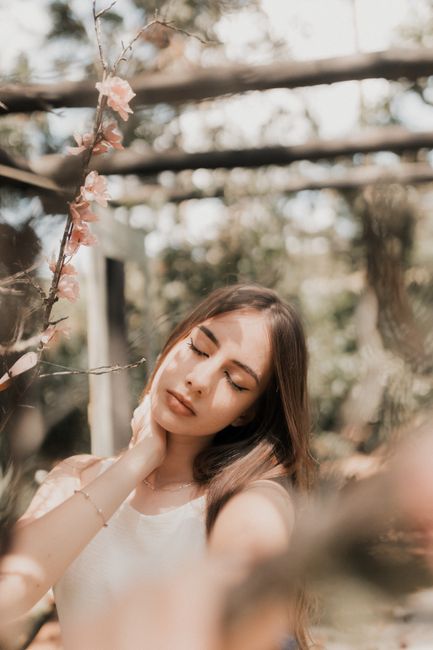 Peaceful woman posing outdoors surrounded by flowers.