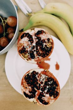 Close-up of halved pomegranate on plate with bananas and grapes. Perfect for healthy lifestyle concepts.