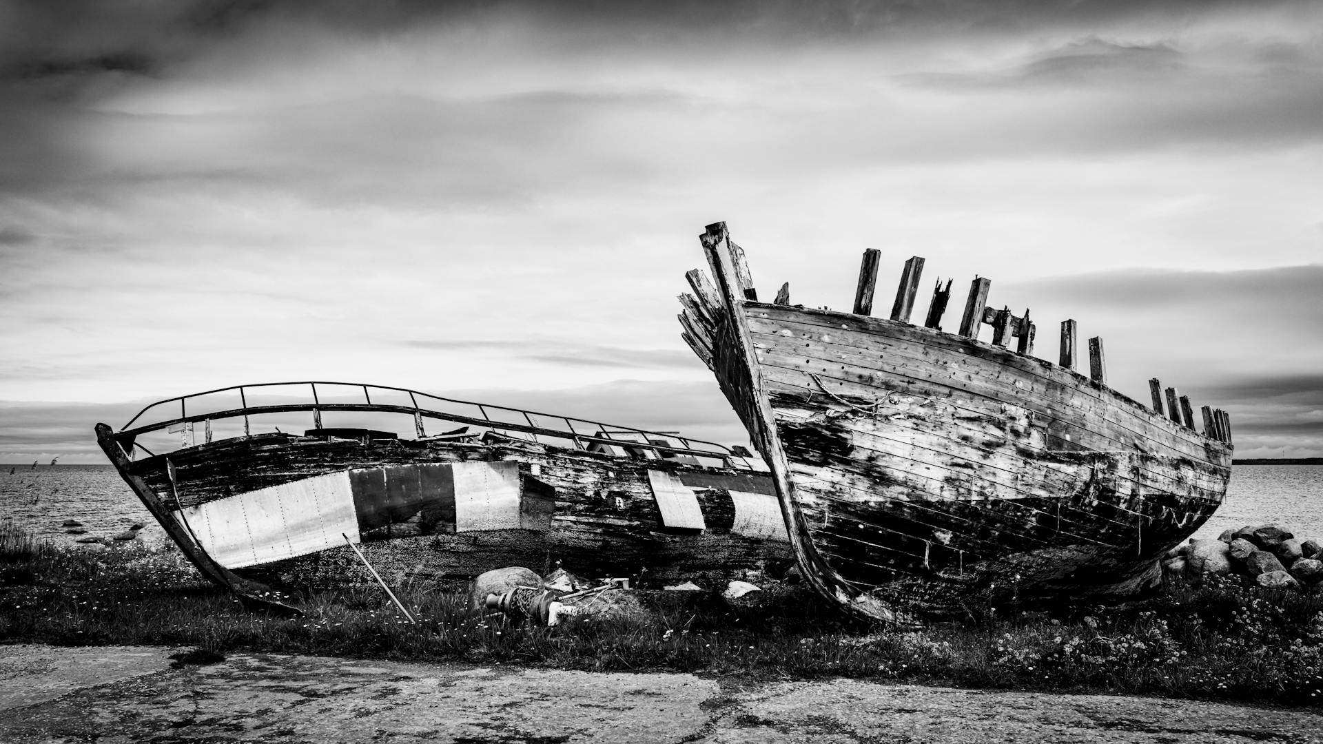 Dramatic black and white photo of an abandoned shipwreck on a rocky shore under a cloudy sky.