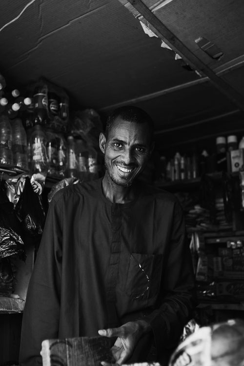 Free A black and white portrait of a smiling man in a bustling Abuja market. Stock Photo