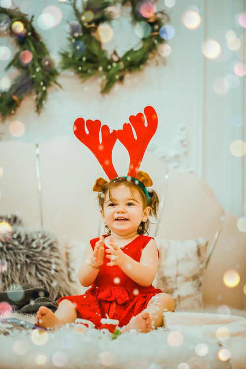 Free Cute child wearing reindeer antlers sits happily in a festive holiday setting. Stock Photo